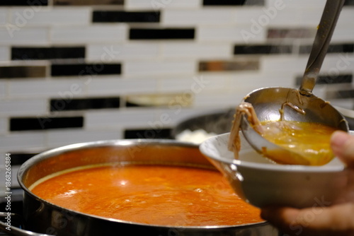 A close-up shot of Gaziantep's famous beyran soup being poured from the pot into bowls with a ladle. Steam rises as the soup cooks. Beyran is made with rice, lamb meat, and vinegar. Ramadan, iftar.