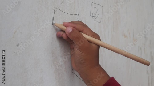 a small boy's hand is drawing or scribbling on a white wall using a simple wooden pencil