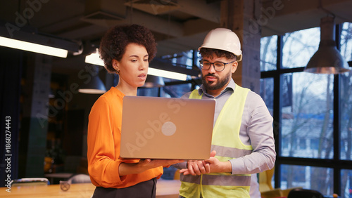 Female architect and male builder in hard hat reviewing building planning on laptop business concept