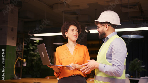 Female architect and male builder in hard hat reviewing building planning on laptop business concept