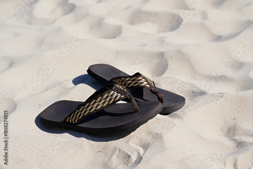 Dark brown men's flip-flops on a sunny summer sandy beach