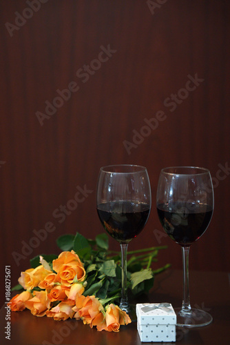 A romantic setting with two glasses of red wine and a bouquet of peach roses.