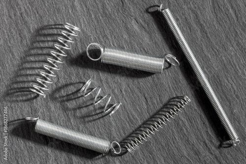 Assorted metallic tension springs arranged on a dark slate background, ideal for industrial, mechanical, or engineering themes.