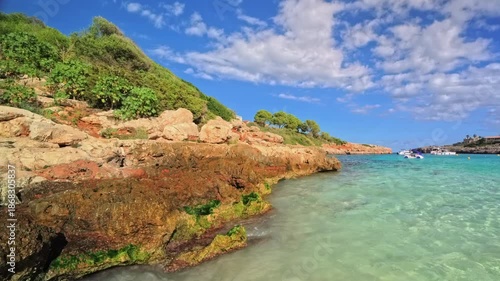 PORTOCOLOM, MALLORCA, SPAIN - OCTOBER 24, 2025: Clear water and rocky shores of Cala Marsal in Portocolom, Mallorca on a sunny day, beautiful coastline and colors