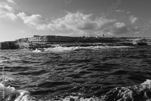 Black and white seascape of rugged rocky coastline with waves breaking against shore, emphasizing contrast, textures and raw coastal nature in a timeless fine art style.