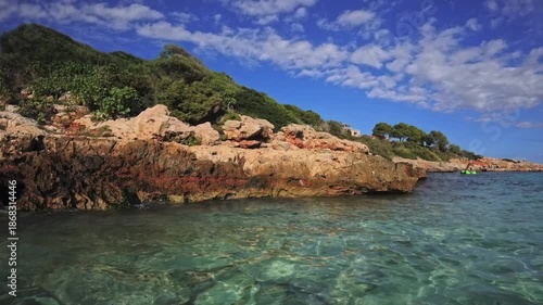 PORTOCOLOM, MALLORCA, SPAIN - OCTOBER 24, 2025: Sunny autumn day at Cala Marsal beach, clear turquoise water meets a rocky coastline with green vegetation