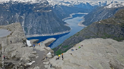 Tourists walking on rocky plateau near Trolltunga above Ringedalsvatnet in Norway. Hikers explore dramatic fjord scenery during an active mountain adventure.