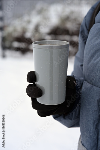 Person holding reusable eco-friendly cup with hot beverage outdoors in winter. Concept of sustainable lifestyle, zero waste, environmentally friendly habits, warmth, cold weather, and conscious consum