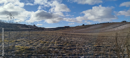 Paisaje rural de campos cultivados bajo un cielo azul intenso con nubes blancas y restos de escarcha invernal en Burgos, España