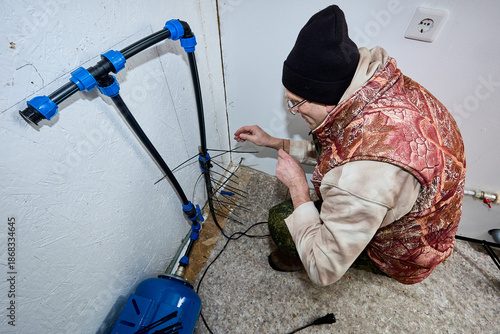 While preparing country house for winter frosts homeowner installs heating cable on incoming pipe.