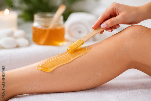 A woman leg as she applies warm honey colored wax with a wooden spatula for hair removal