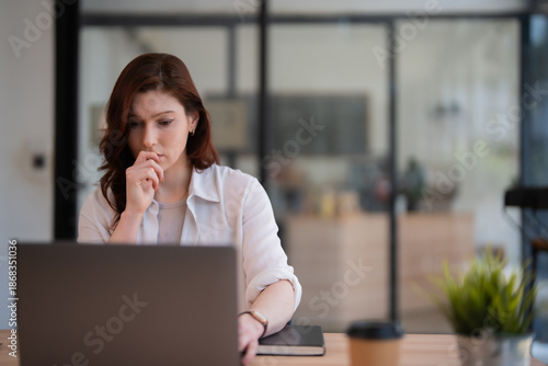 Canvas Print Young professional businesswoman concentrating and analyzing data on her laptop,