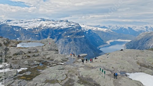 Tourists walking across rocky plateau near Trolltunga in Norway. Hikers explore the exposed mountain terrain with fjord views in the distance.