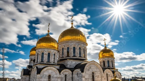 Stunning golden domed Orthodox church under a bright blue sky with clouds and sunburst shining