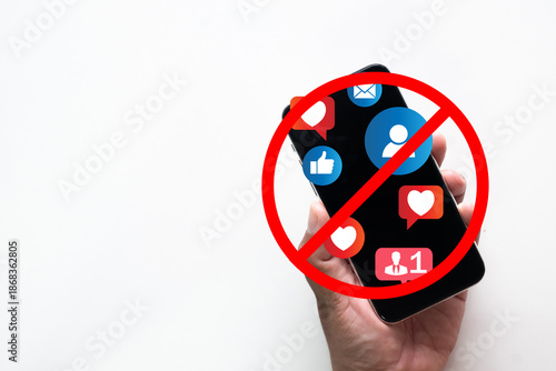 Hand holding smartphone with social media icons and red forbidden sign. Concept of digital detox, stopping internet addiction, social media ban, mental health awareness, and disconnection on white.
