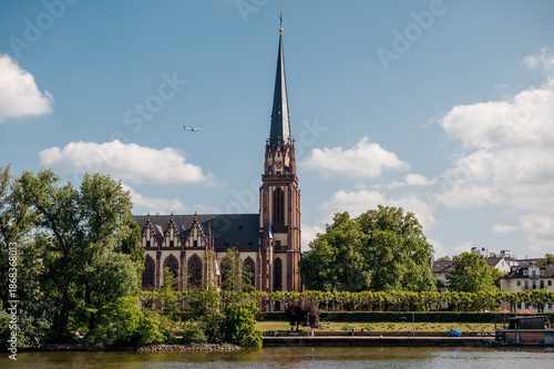 Frankfurt am Main cathedral spire and riverfront with an airplane flying in the sky