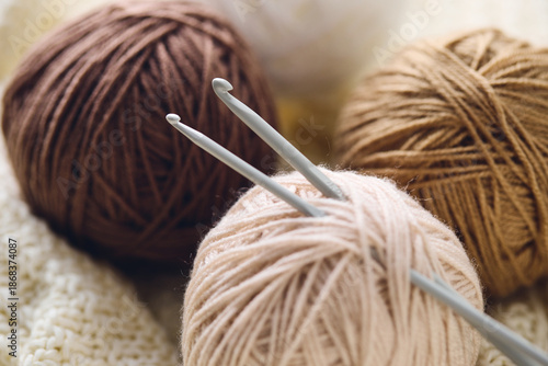 Photography Crochet hooks and balls of beige and brown yarn on white knitted background