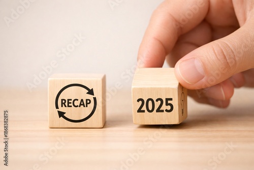 Hand placing the 2025 block near the Recap symbol cube, annual anlysis of the economy and business agreement review, valuable for financial reports