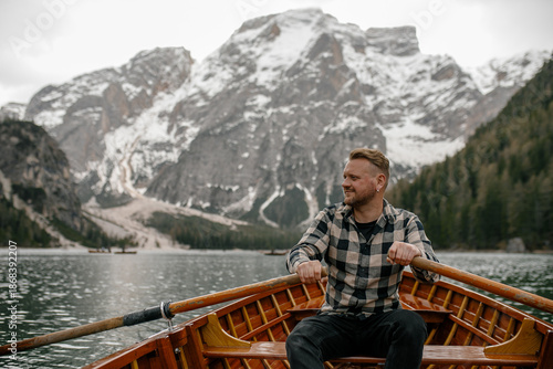 Man rowing wooden boat on Braies Lake with snowy mountains in background