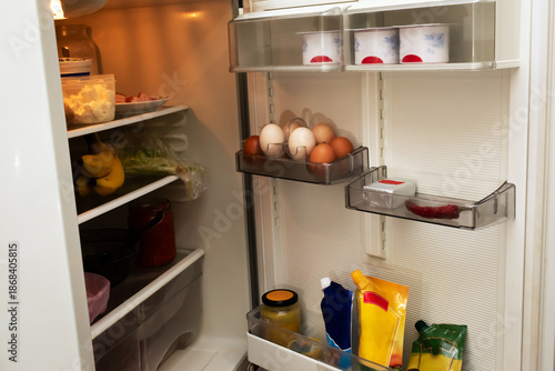 Inside view of an open domestic refrigerator with various food products and eggs on the door shelves