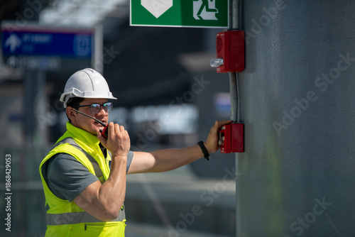 Engineer wearing safety unifrom and helmet under checking fire alarm emergency system in industry factory and exit door is factory security protection concept.	
