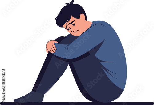A sad man sitting on the floor with his head down and arms around his knees feeling depressed