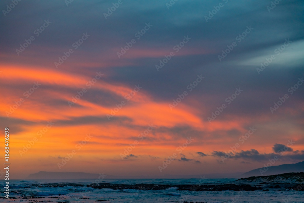 Obraz premium Dramatic Golden sunset over tranquil beach, waves lashing the pebble coastline