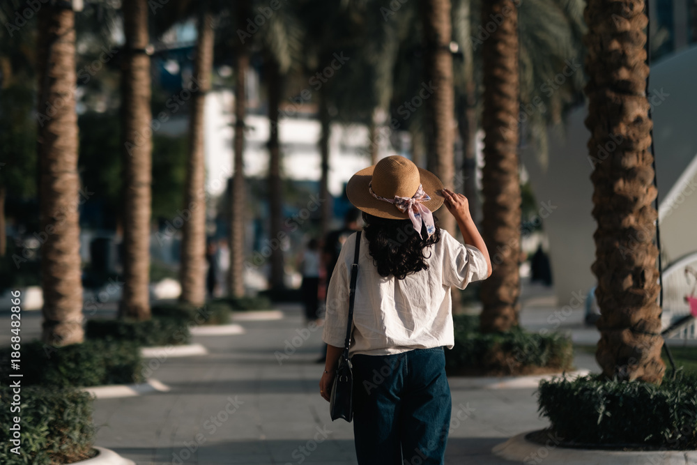 Fototapeta premium Tourist woman walking through palm trees in public park enjoying Dubai city travel