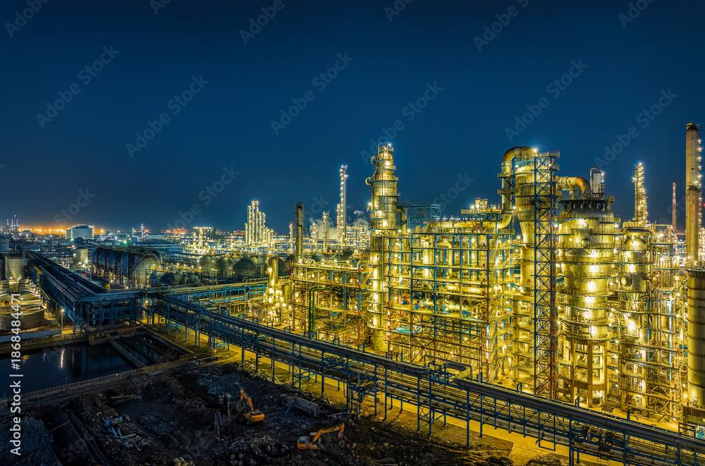 Fototapeta premium Illuminated oil refinery chemical plant with complex pipe systems and storage tanks at night.