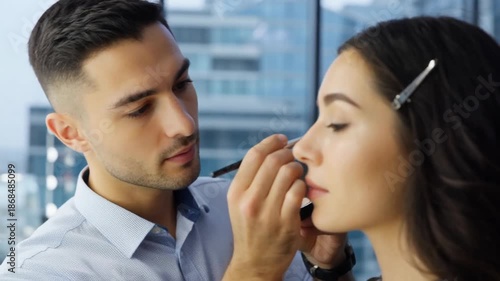 Professional makeup artist applying makeup to a woman in a modern city setting with large windows in a stylish environment