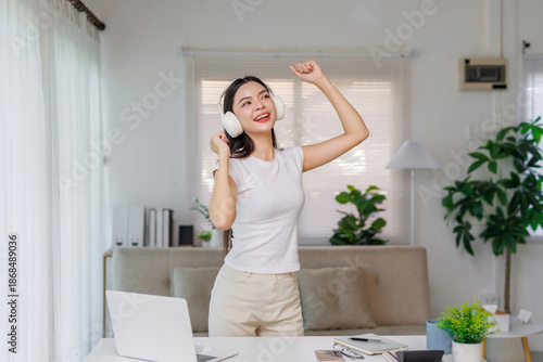 Happy asian woman wearing headphones, listening to music and dancing at home, mixing work from home with relaxation