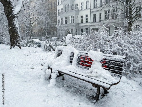 Snowman and Snowdog sitting on a bench in Berlin Kreuzberg on a snowy winter day at Grimmstrasse park.