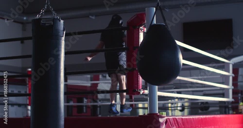 Against soft gym light, the boxer's silhouette flows effortlessly, combining strength and determination in a rhythmic jump rope session. Slow motion zoom out 4K footage.