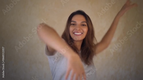 A young woman happily gesturing with her arms outstretched in a beige room