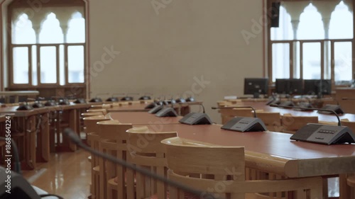 Empty conference room featuring wooden tables and professional microphones for business meetings. Rows of chairs in vacant boardroom of university or government office building environment.