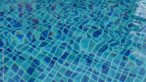 Footage of clean blue swimming pool water with gentle ripples and sunlight reflections. Abstract calm water texture background ideal for summer,wellness, relaxation,travel,luxury, and resort concepts.