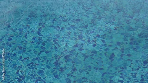Footage of clean blue swimming pool water with gentle ripples and sunlight reflections. Abstract calm water texture background ideal for summer,wellness, relaxation,travel,luxury, and resort concepts.