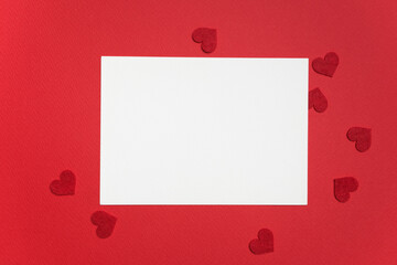 Blank greeting card mockup on red background surrounded by small red heart shapes, perfect for Valentine's Day design projects and romantic messages with copy space
