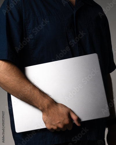 Cropped view of a man holding a closed modern laptop, representing technology, business, and mobile work.