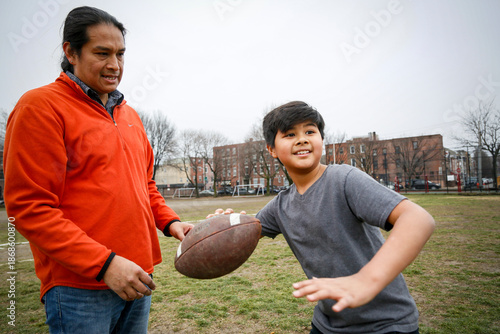 Philadelphia, Pennsylvania, USA. Native American father teaching his young son how to throw a football