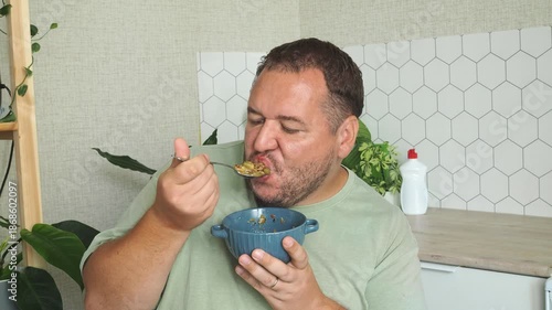 A man is eating soup in his kitchen.
