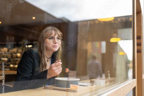 Woman eating a fresh salad in a modern restaurant, enjoying her lunch break looking out the window