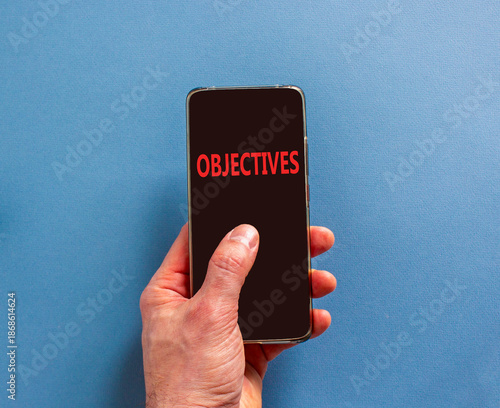 Objectives symbol. Concept word Objectives on beautiful cell phone's screen in businessman's hand. Beautiful blue background. Business objectives concept. Copy space.