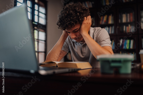 Foto Tired student studying with book and laptop in library