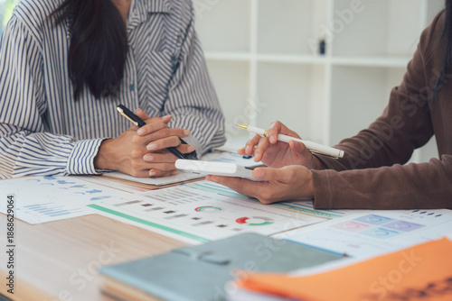 Financial Strategies: Two professionals collaborate, examining charts, documents, and a calculator on a desk, possibly during a financial review. The scene reflects teamwork and problem-solving.