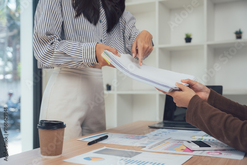 Document Exchange in the Workplace: In a modern office setting, one person's hand reaches to receive documents from another, symbolizing efficient communication and collaborative efforts. 