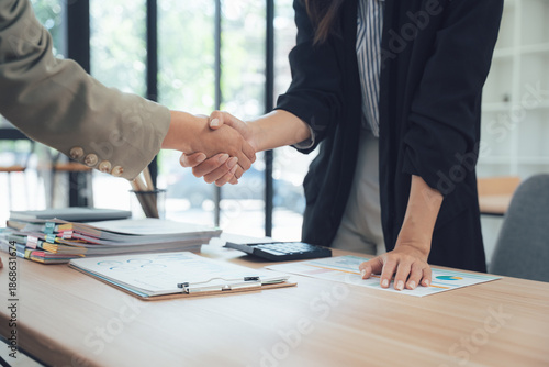 Handshake Deal: A formal handshake seals a successful business deal, symbolizing agreement, trust, and partnership, set against a modern office background.
