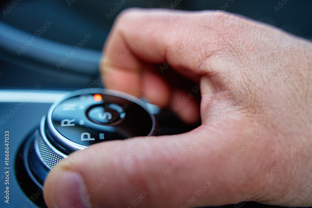 Fototapeta premium Close up of hand turning car automatic transmission selector knob inside vehicle. Driver turning rotary gear shift in drive mode