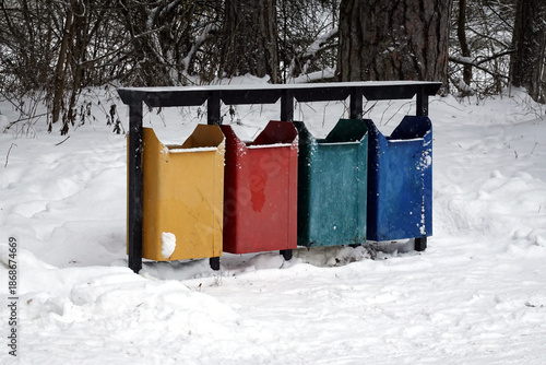 Row of colorful recycling bins standing in snowy winter forest front view closeup