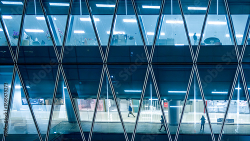 Modern glass office building interior seen through geometric facade in Hong Kong, China. Abstract corporate workplace with anonymous silhouettes symbolizing business activity and organization